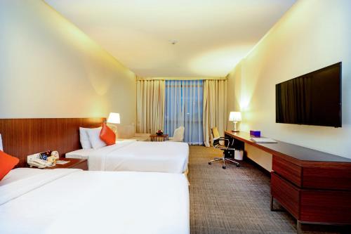a hotel room with two beds and a desk and a television at Becamex Hotel New City in Thu Dau Mot