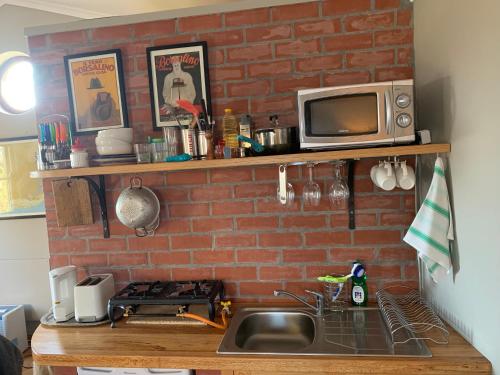 a kitchen with a brick wall and a sink and a microwave at Sapphire Studio in Noordhoek