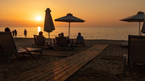 a group of people sitting on the beach watching the sunset at Acharavi Beach Hotel in Acharavi