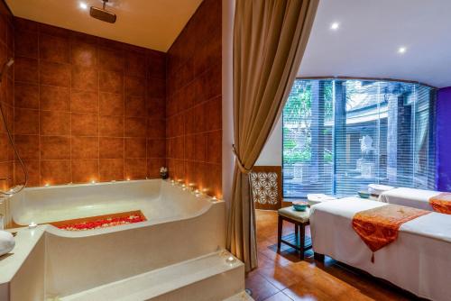 a bathroom with a tub and a bed and a window at VOUK Hotel and Suites Nusa Dua Bali in Nusa Dua