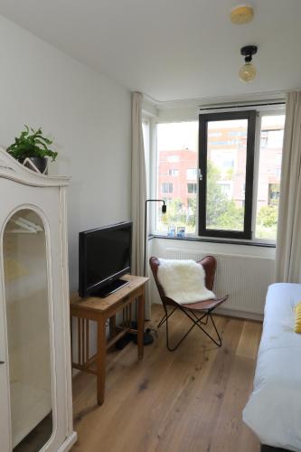 a living room with a television and a desk with a chair at B&B De Zwanebloem in Amsterdam