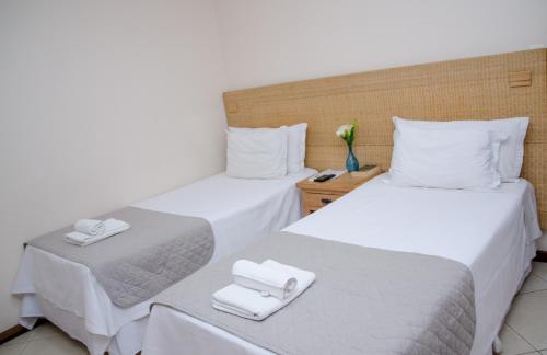 two beds in a room with white sheets and towels at Hotel Pousada La Belle in Itaguaí