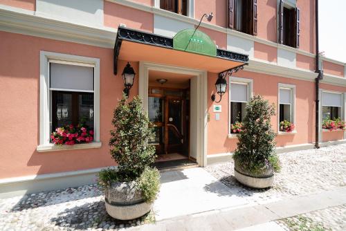 a pink building with two potted plants in front of it at Hotel Spessotto in Portogruaro