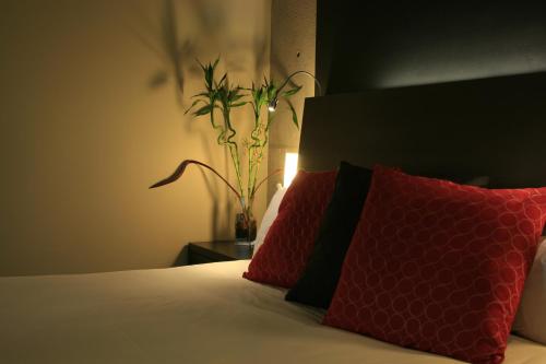 a bedroom with a bed with two red pillows and a plant at Grand Times Hotel in Quebec City