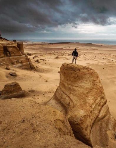 a man standing on a large rock in the desert at villa tunis village in ‘Izbat an Nāmūs