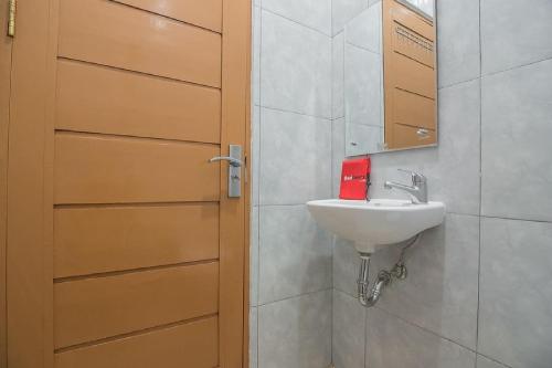 a bathroom with a sink and a wooden door at RedDoorz Plus near Syamsudin Noor Airport 3 in Banjarbaru