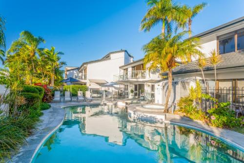 a swimming pool in front of a house with palm trees at Noosa Boutique Apartments & Elkhorn Villas in Noosa Heads