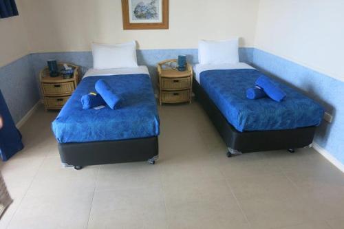 two beds in a room with blue sheets and blue pillows at The Sunset in Flying Fish Cove