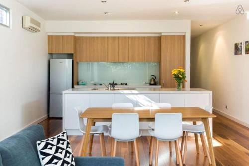 a kitchen with a wooden table and white chairs at Bradman Modern Style a Walk to MCG, Swan St, CBD in Melbourne
