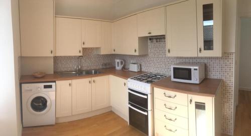 a kitchen with white cabinets and a stove and a microwave at Arran Ferry Apartment in Ardrossan
