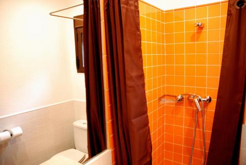 uma casa de banho com um chuveiro em azulejos laranja e um WC. em Hostal El Cardenillo em Madrigal de la Vera