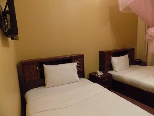 two beds in a small room with white sheets at Belline Hotel Ishaka in Ishaka