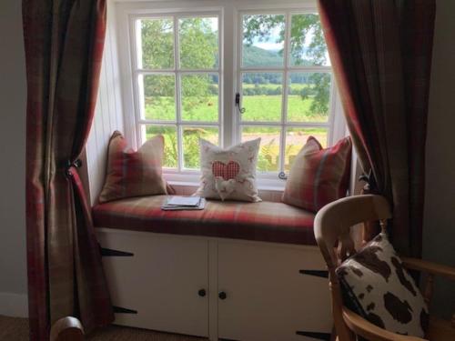 a window seat with pillows sitting in front of a window at Glencroft A Fairytale Highland Cottage in Aberfeldy