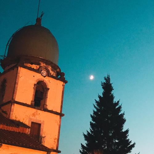 una torre del reloj con un árbol y la luna en el cielo en La casina del Indiano, en Malleza