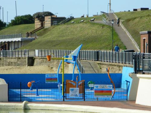 a blue fence with a playground next to the water at 'Pavilion Cottage' next to Gorleston beach with sea views - pet friendly! in Gorleston-on-Sea