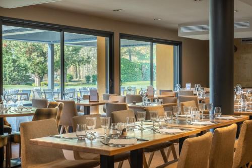 a row of tables and chairs in a room with windows at Domaine du Gouverneur, Hôtel, Restaurant & Golf in Monthieux