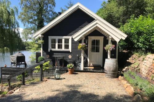 a small black cottage with a patio next to the water at Sommerhus i idylliske omgivelser in Veksø