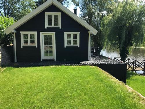 a black house on the water with a green lawn at Sommerhus i idylliske omgivelser in Veksø