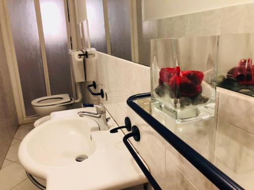 La salle de bains est pourvue d'un lavabo et d'un vase de fleurs rouges. dans l'établissement Cinque terre SUITE, à La Spezia