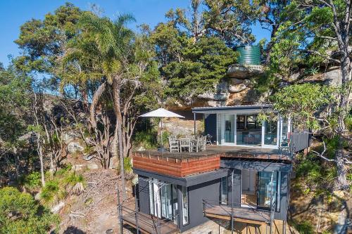 a house on top of a hill with trees at Cape Mackerel Cabin with Magic Palm Beach & Pittwater Views in Great Mackerel Beach