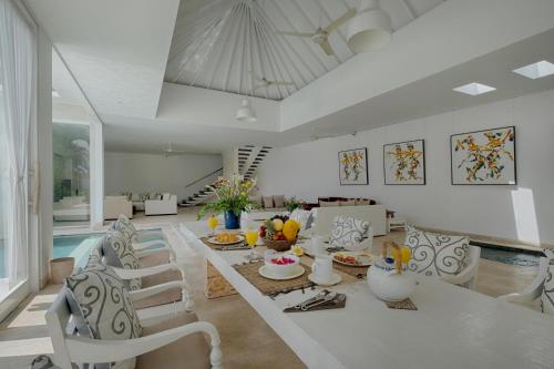 een woonkamer met witte stoelen en een tafel met eten bij Canggu Villa by Sanga Sanga Hospitality in Canggu