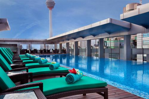 uma piscina de hotel com cadeiras verdes e um edifício em PARKROYAL Serviced Suites Kuala Lumpur em Kuala Lumpur