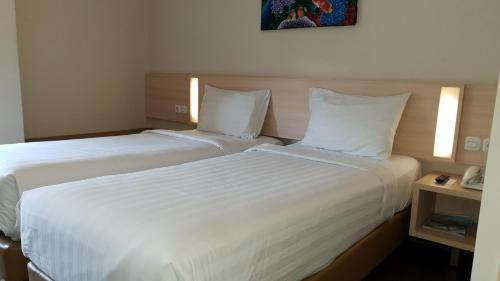 two beds in a hotel room with white sheets at BIZ HOTEL City Center in Ambon