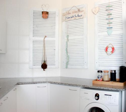 a white kitchen with a washing machine and windows at Lagoon Beach Neptune Isle Cape Town in Cape Town
