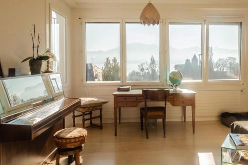 a living room with a desk and a table and windows at La Maison des Copains in Blonay