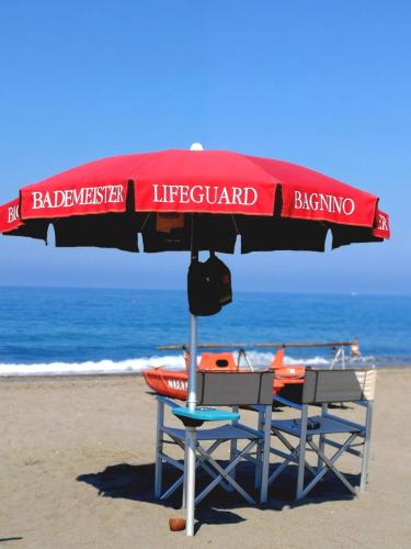 a lifeguard umbrella and two chairs on the beach at CSA Hotel Beach & Park in Marina di Bibbona