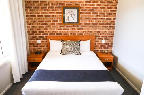 a bed in a room with a brick wall at Akuna Motor Inn and Apartments in Dubbo