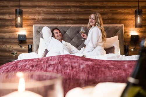 a man and woman laying in bed with a glass of wine at BAD MOOS - Aqua Spa Resort in Sesto