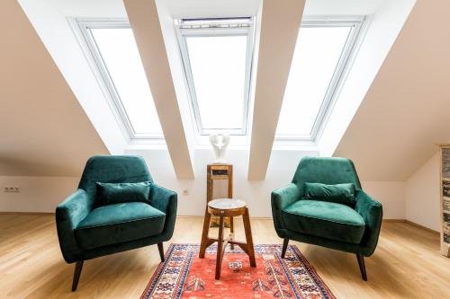 2 grüne Stühle und ein Tisch in einem Zimmer mit Fenstern in der Unterkunft Große Dachgeschosswohnung im Herzen von Graz in Graz