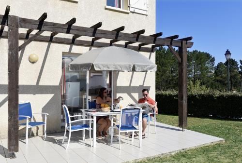 two people sitting at a table under an umbrella at Résidence Odalys Les Hauts de Salavas in Salavas