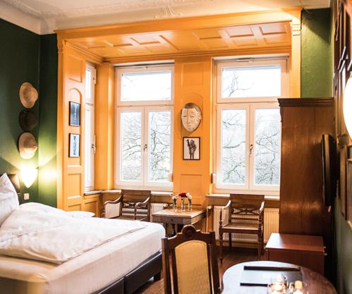 a bedroom with a bed and a table and windows at Hotel Ritzi in Munich