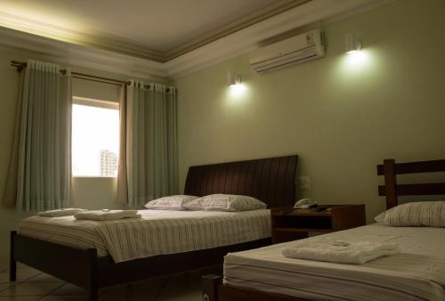 a hotel room with two beds and a window at Hotel Barão Do Rio Branco in Bebedouro