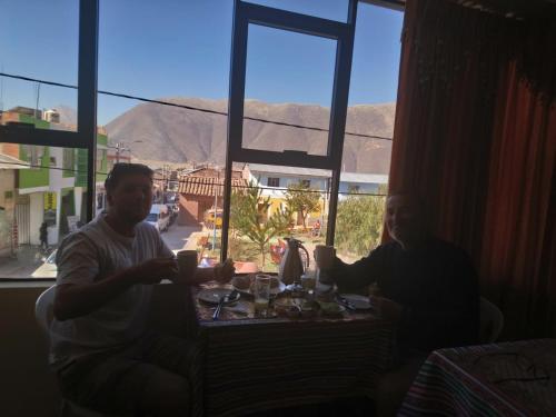 two men sitting at a table with drinks in front of a window at Hostal Inca in San Pedro