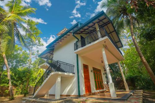 a house with a balcony and palm trees at Riverview Cabana Tissamaharama in Tissamaharama