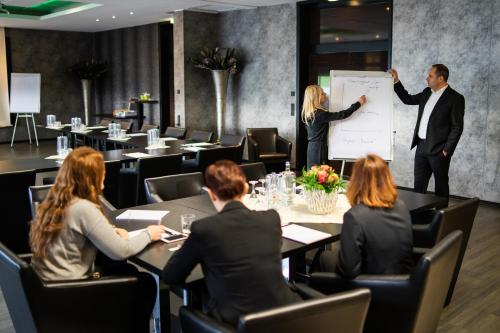 a man giving a presentation in a room with people sitting at tables at salinenparc Design Budget Hotel in Erwitte
