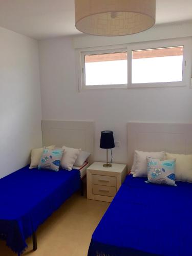 two beds in a room with blue sheets and a window at Fairway View Penthouse in Murcia