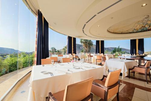 Un restaurante con mesas y sillas blancas y grandes ventanales. en Hotel Envia Almería Spa & Golf, en Aguadulce