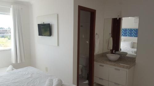 een witte badkamer met een wastafel en een spiegel bij Condomínio Mar da Galiléia - Apto 27 in Porto Seguro