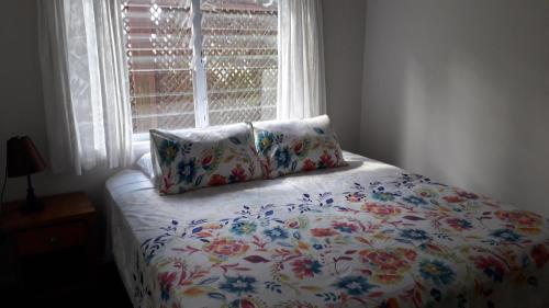 a bed with a floral comforter with a window at Te Akapuao Studio Villas in Rarotonga