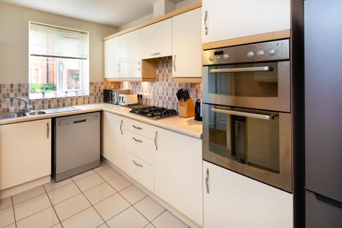 a kitchen with white cabinets and stainless steel appliances at Modern and Spacious Home From Home 1 mile from M1 - with Netflix, Prime Video, PS5, free parking, superfast WiFi, BBQ - Sleeps 11 - By Brightleap Apartments in Milton Keynes