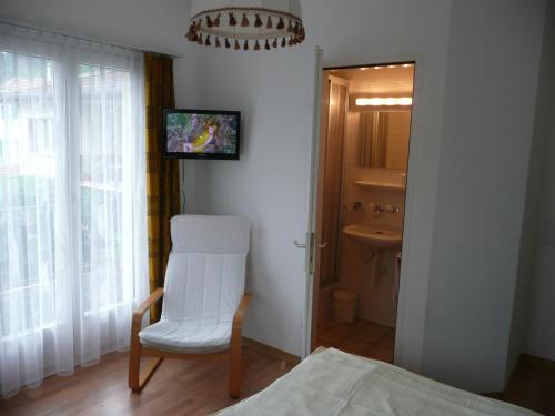 a bedroom with a white chair and a bathroom at Hotel Adelboden in Wikon