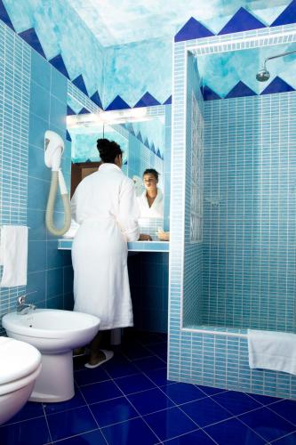 a woman in a blue bathroom with a sink at Hotel Marini in Sassari