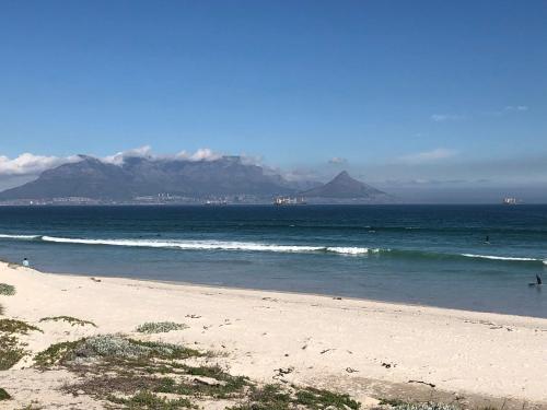 a beach with mountains in the background and people in the water at The Little Palm in Bloubergstrand