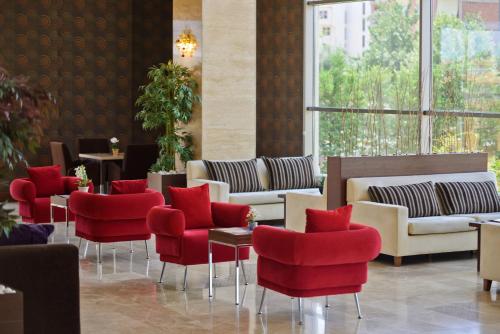 a lobby with red chairs and tables and windows at North Point Hotel in Denizli