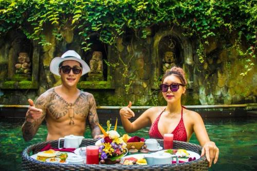 Un uomo e una donna seduti in acqua con un tavolo di cibo di Arma Museum & Resort ad Ubud