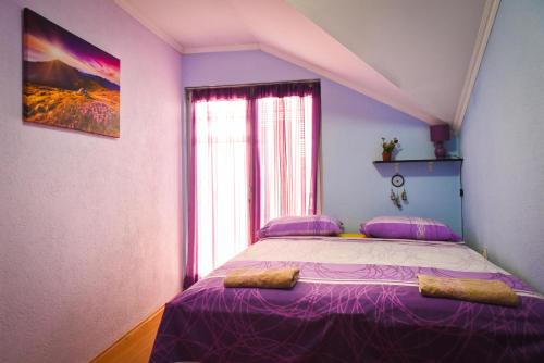 sypialnia z łóżkiem z fioletową pościelą i oknem w obiekcie Goldy Hostel w mieście Bitola